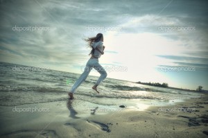Beautiful young sport woman running on water at sea coast. Sunset with dramatic sky