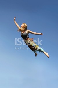 A young woman is jumping up as if flying through the air in front of a blue sky background.