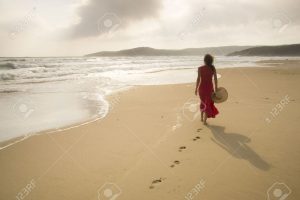 14786845-jeune-femme-marcher-sur-une-plage-d-serte-sauvage-vers-des-faisceaux-de-lumi-re-c-lestes-qui-tombent-banque-dimages